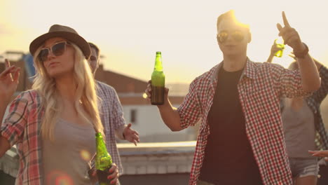 Young-couple-in-playd-red-shirt-and-trendy-glasses-move-in-a-dance-with-beer-at-a-party-with-their-friends.